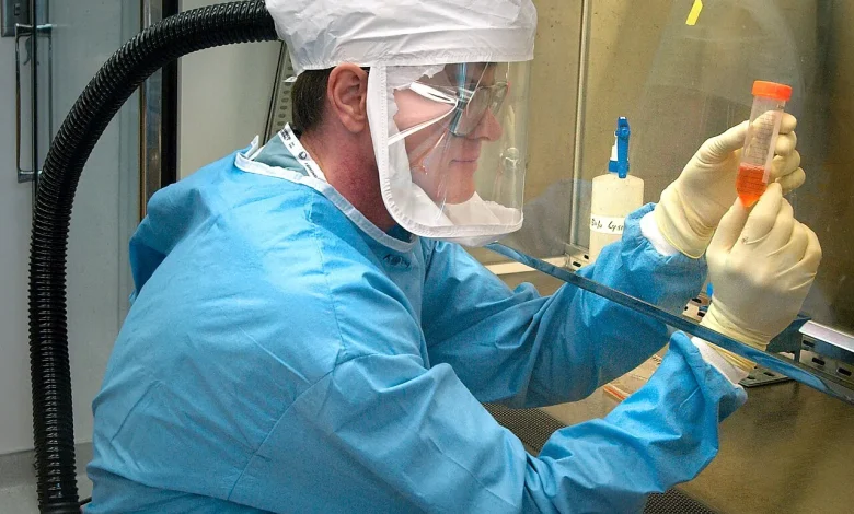 Scientist in protective clothing holding a sample in a virus laboratory